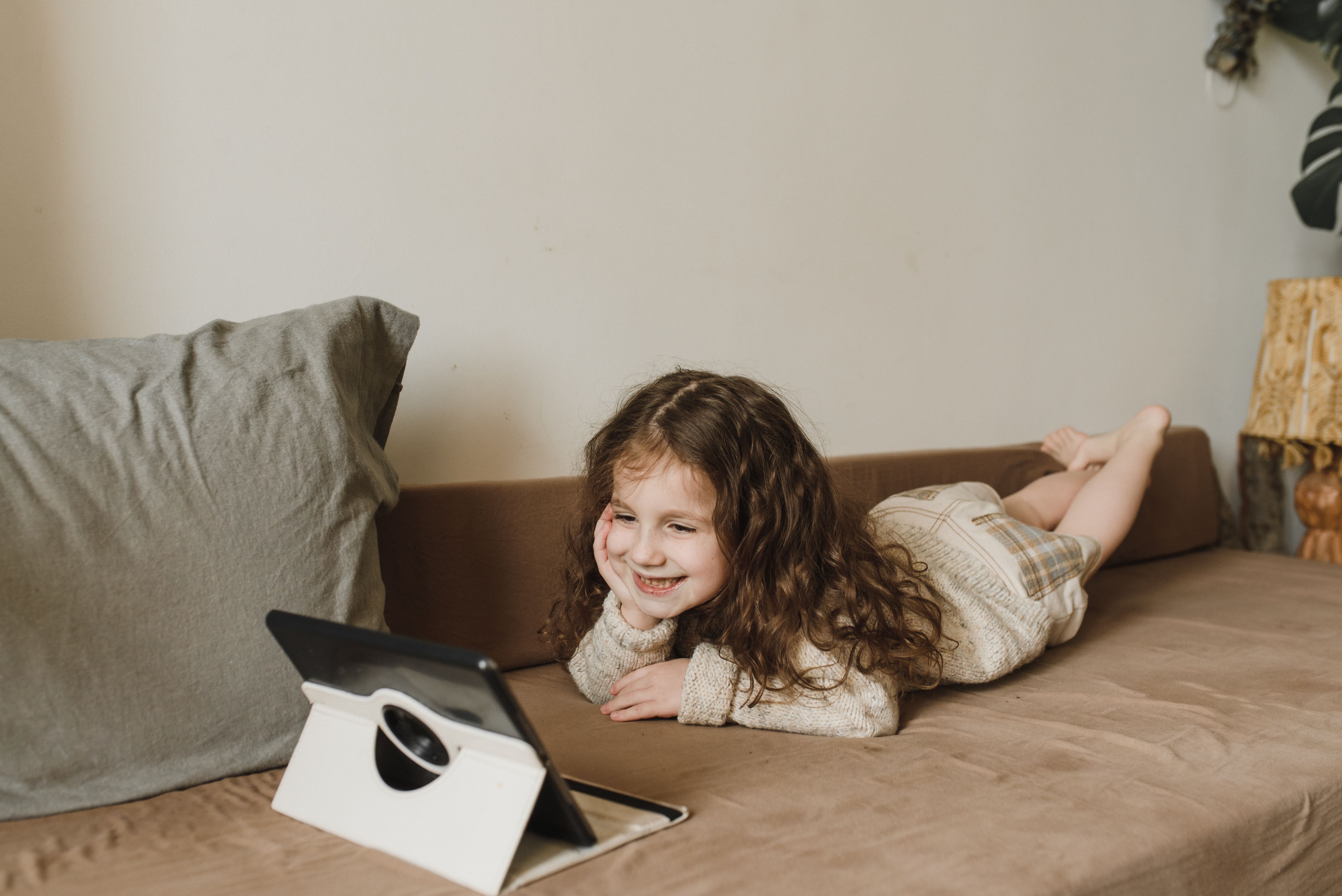 A girl lying on a sofa, smiling at a tablet